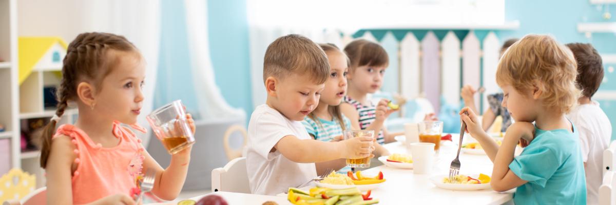 Kleinkinder sitzen an einem Tisch in einem hellen Zimmer und essen gemeinsame Obst und Gemüse
