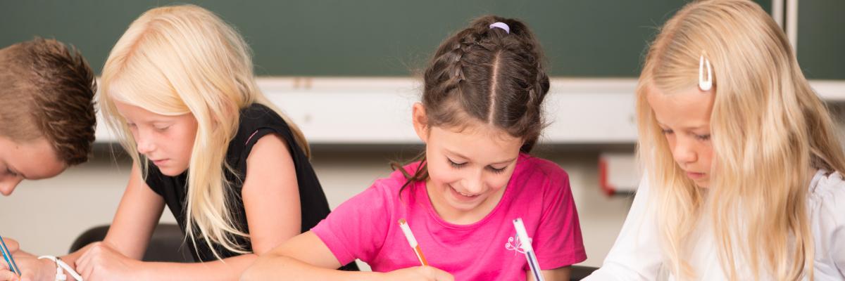 Drei Grundschulkinder sitzen an einem Schultisch und lernen