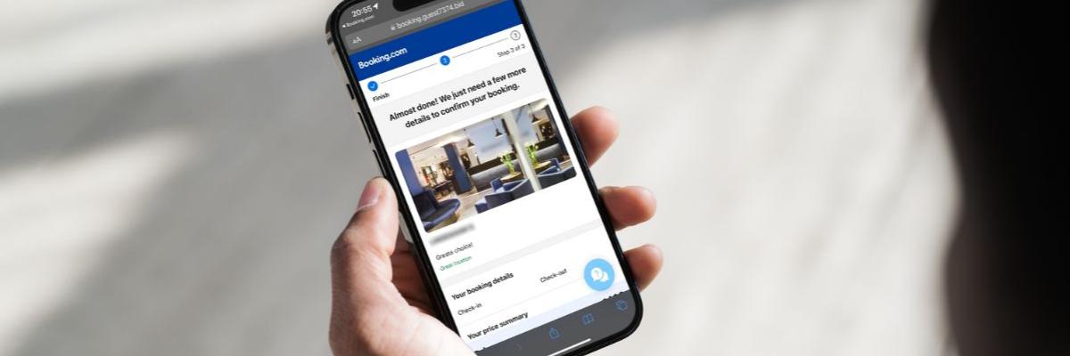 Smartphone in einer Hand, auf dem Display ist eine Internetseite zu sehen, die booking.com ähnelt.