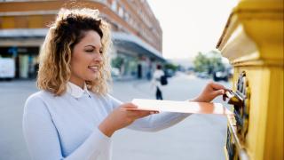 Frau lächelt und wirft ein Brief in den Briefkasten