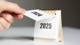 Hand reißt Kalenderblatt ab, sodass Jahreszahl 2025 zum Vorschein kommt