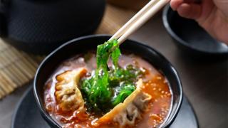 graue Schale, aus der mit Stäbchen Algensalat gegessen wird