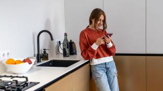 Junges Mädchen lehnt mit Smartphone in der Hand an einer Küchenzeile