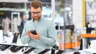 Mann sucht Smartphone in Elektronikmarkt aus