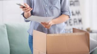 Frau hält Smartphone und öffnet ein Paket