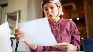 Eine junge Frau hält mit besorgtem Gesicht einen Brief in der Hand und liest 