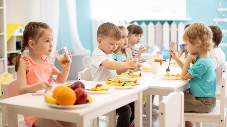 Kleinkinder sitzen an einem Tisch in einem hellen Zimmer und essen gemeinsame Obst und Gemüse