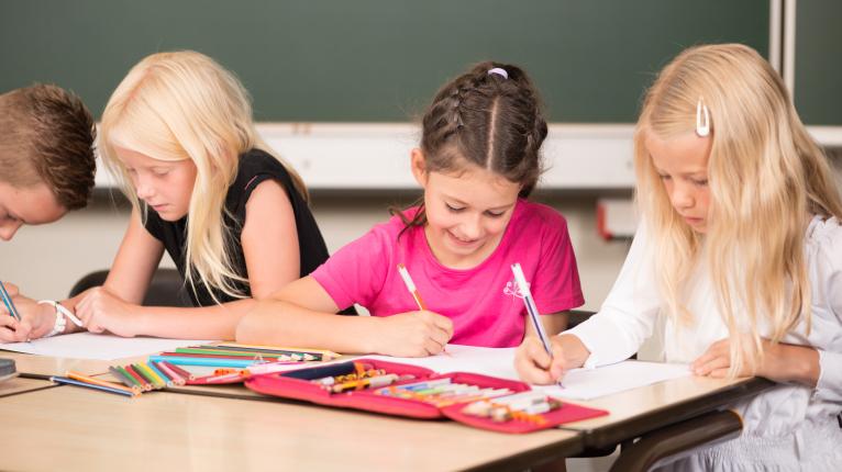 Drei Grundschulkinder sitzen an einem Schultisch und lernen