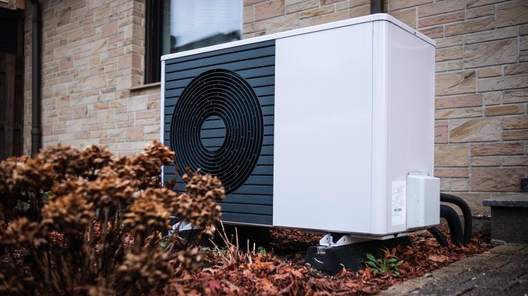 Wärmepumpe vor Hauswand mit Herbstlaub